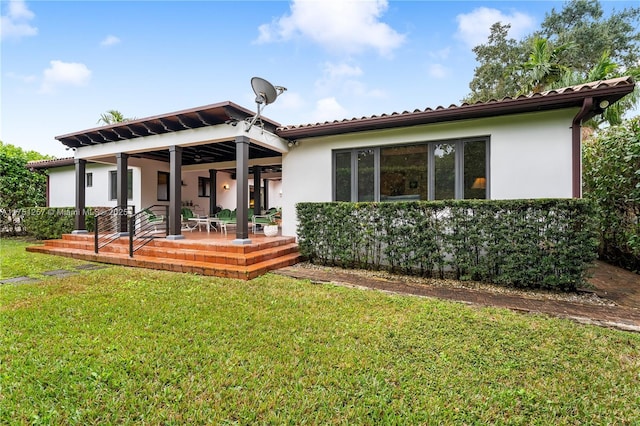 rear view of property featuring a patio area, a lawn, and stucco siding