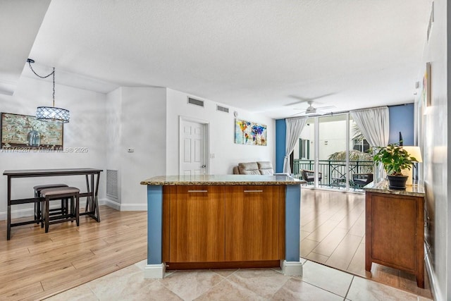 kitchen featuring brown cabinetry, stone countertops, and visible vents