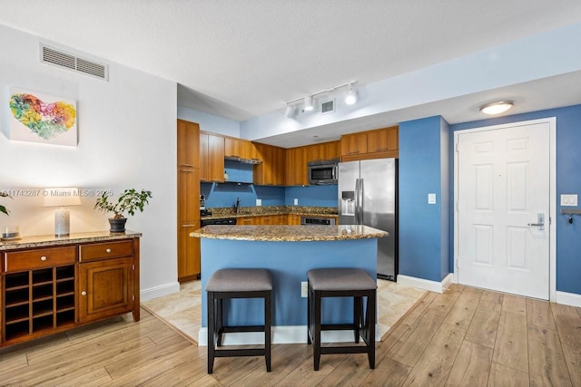 kitchen featuring appliances with stainless steel finishes, brown cabinetry, light wood-style floors, and visible vents