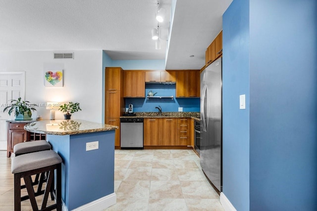 kitchen with stone counters, stainless steel appliances, a breakfast bar, a kitchen island, and brown cabinetry