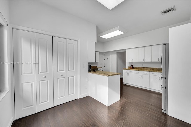 kitchen featuring dark wood-style flooring, visible vents, freestanding refrigerator, white cabinetry, and a peninsula