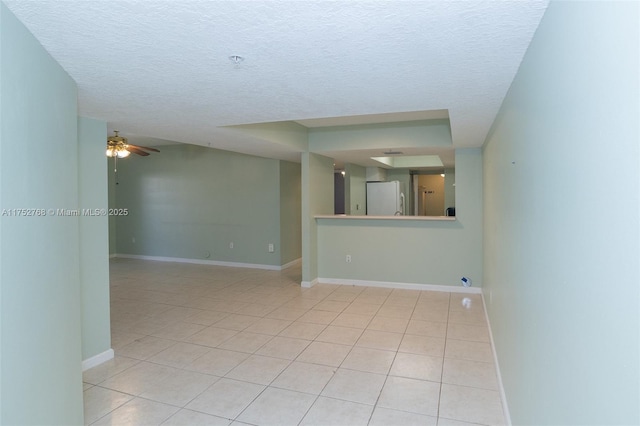 spare room with a textured ceiling, light tile patterned flooring, a ceiling fan, and baseboards