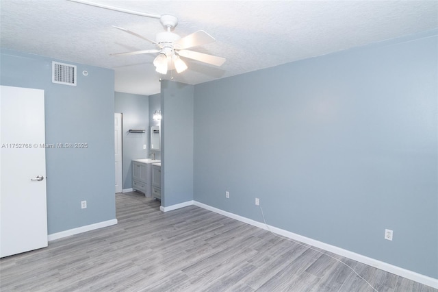 unfurnished bedroom featuring baseboards, visible vents, ensuite bathroom, a textured ceiling, and light wood-type flooring