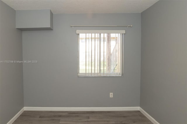 spare room with a textured ceiling, baseboards, and wood finished floors