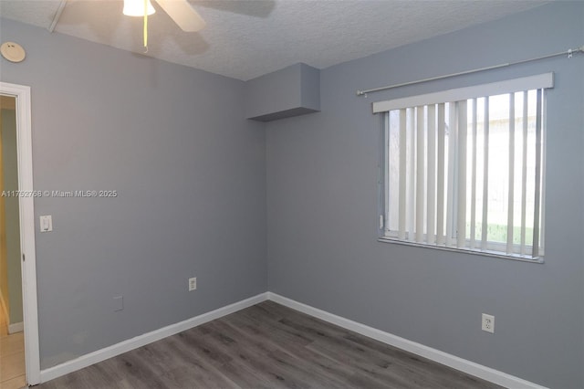 empty room with a wealth of natural light, a textured ceiling, baseboards, and wood finished floors