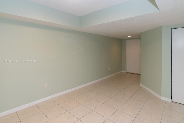 spare room featuring baseboards, a textured ceiling, and light tile patterned flooring