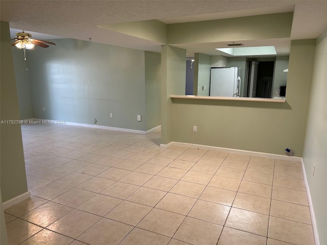 unfurnished room with light tile patterned floors, ceiling fan, a textured ceiling, and baseboards