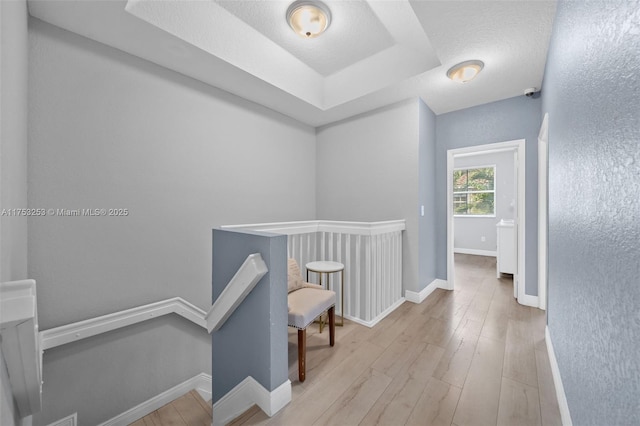 corridor with a textured ceiling, baseboards, wood finished floors, and an upstairs landing