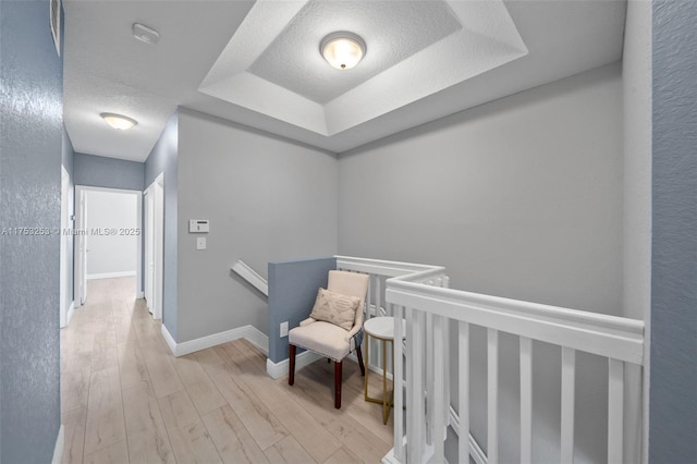 hall featuring a raised ceiling, a textured ceiling, an upstairs landing, wood finished floors, and baseboards