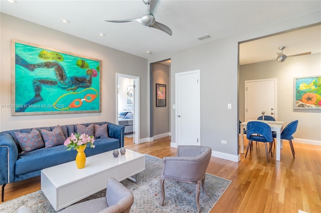 living area with baseboards, light wood-style flooring, visible vents, and a ceiling fan