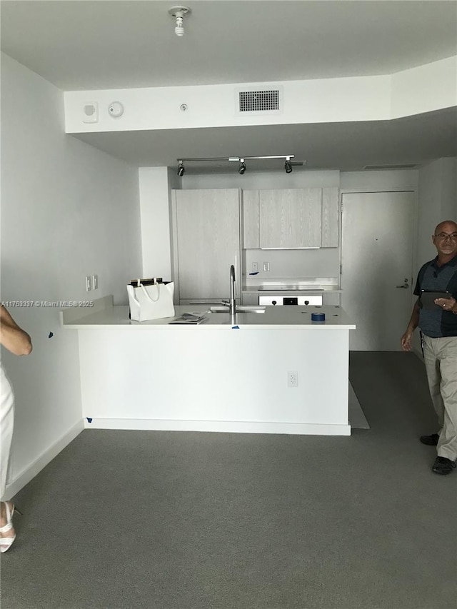 kitchen with baseboards, visible vents, a peninsula, a sink, and light countertops