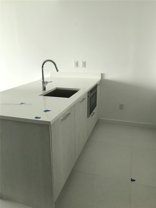 kitchen featuring modern cabinets, a sink, light tile patterned flooring, light countertops, and built in microwave