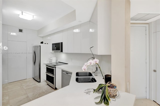 kitchen with stainless steel appliances, light countertops, white cabinets, a sink, and modern cabinets