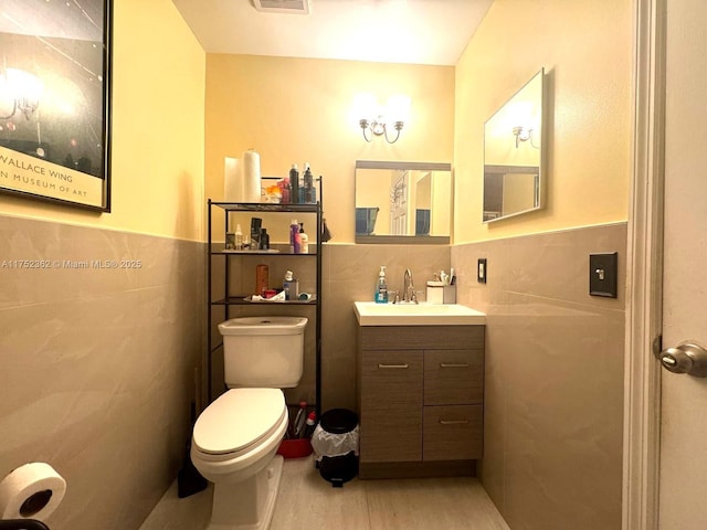 half bathroom with toilet, vanity, tile walls, and wainscoting