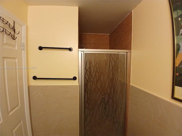 bathroom with a wainscoted wall, a shower stall, and tile walls