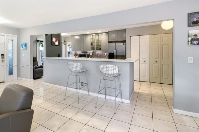 kitchen with light tile patterned floors, stainless steel refrigerator with ice dispenser, gray cabinets, and glass insert cabinets