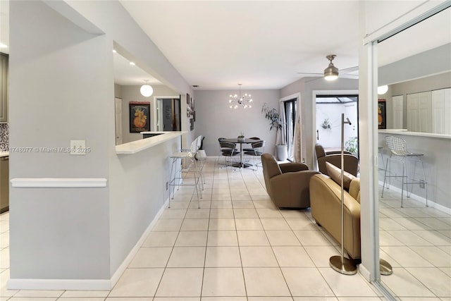 living room featuring light tile patterned floors, baseboards, and ceiling fan with notable chandelier