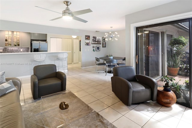 living room with light tile patterned floors, baseboards, and ceiling fan with notable chandelier