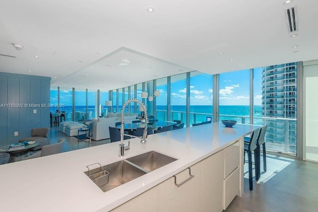 kitchen with visible vents, a water view, a wall of windows, light countertops, and a sink