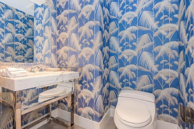 bathroom featuring baseboards, toilet, and wallpapered walls