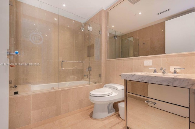 full bath with toilet, tiled shower / bath combo, visible vents, vanity, and tile walls