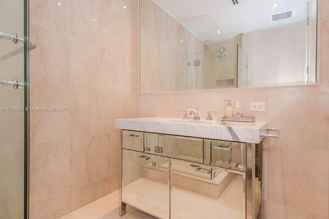 full bath featuring a walk in shower, vanity, visible vents, and tile walls