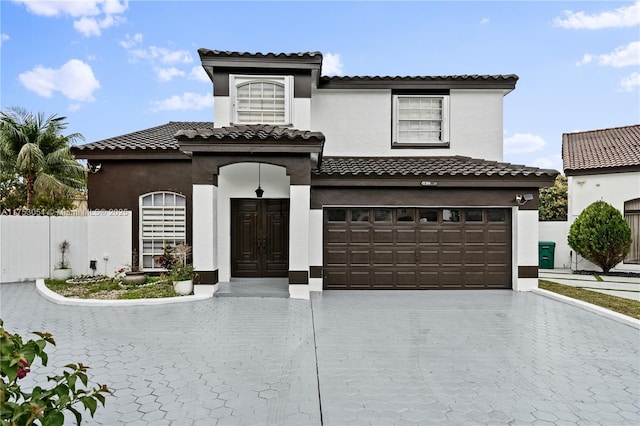 mediterranean / spanish home with decorative driveway, a tile roof, stucco siding, fence, and a garage