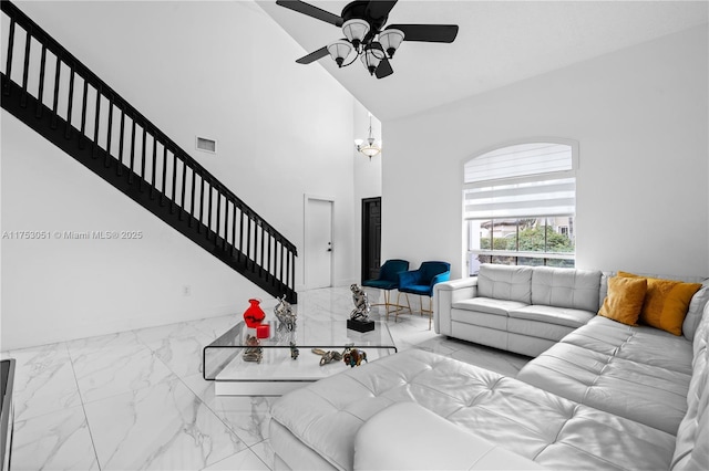 living area featuring visible vents, stairway, marble finish floor, a high ceiling, and ceiling fan with notable chandelier