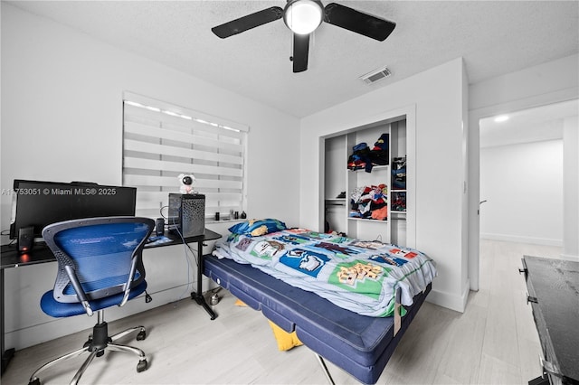 bedroom featuring a ceiling fan, a textured ceiling, visible vents, and wood finished floors