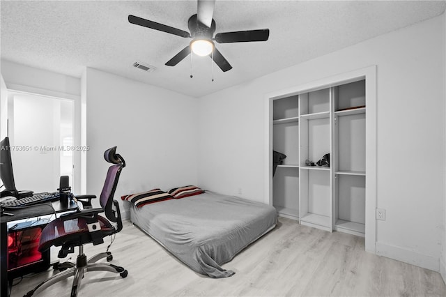 bedroom with a textured ceiling, wood finished floors, visible vents, a ceiling fan, and a closet