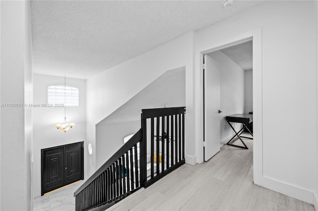 corridor featuring baseboards, a chandelier, a textured ceiling, and wood finished floors