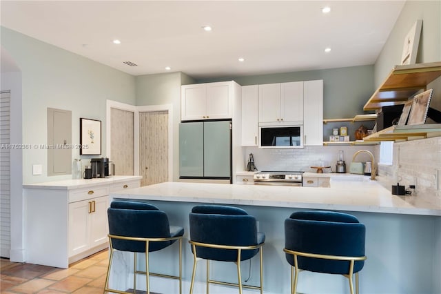 kitchen featuring stainless steel appliances, a peninsula, a sink, backsplash, and open shelves