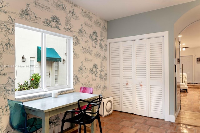 dining space featuring arched walkways and wallpapered walls