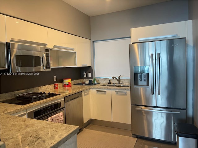 kitchen with light tile patterned floors, appliances with stainless steel finishes, white cabinetry, a sink, and light stone countertops