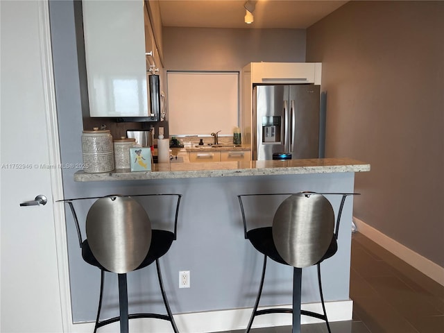 kitchen with white cabinetry, a sink, stainless steel fridge, a peninsula, and a kitchen breakfast bar