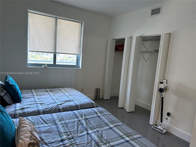 tiled bedroom featuring visible vents, baseboards, and two closets