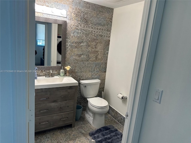 half bathroom with toilet, stacked washer and dryer, tile walls, and vanity