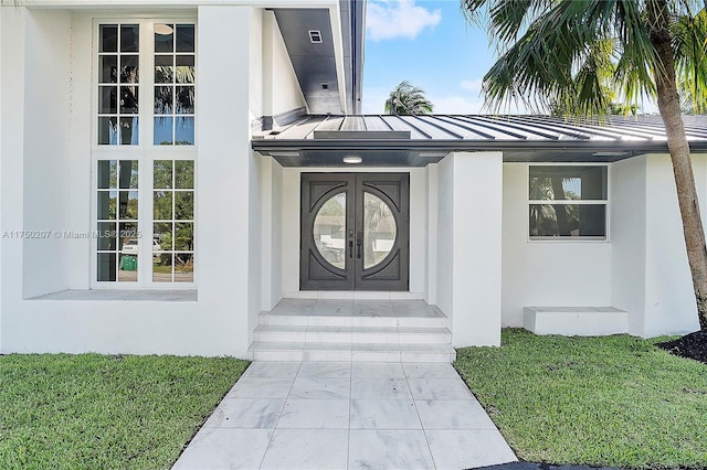 property entrance featuring french doors, a yard, stucco siding, a standing seam roof, and metal roof