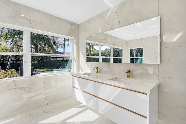 full bathroom with marble finish floor, double vanity, a sink, and tile walls