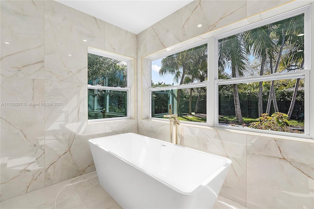 bathroom with marble finish floor, a soaking tub, and tile walls