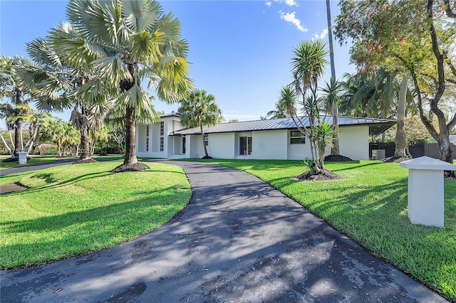 view of front of property with metal roof, driveway, a front yard, and stucco siding