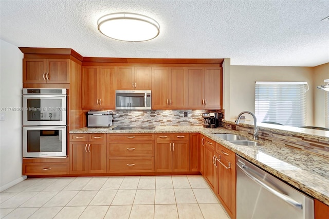 kitchen featuring appliances with stainless steel finishes, brown cabinetry, a sink, and tasteful backsplash