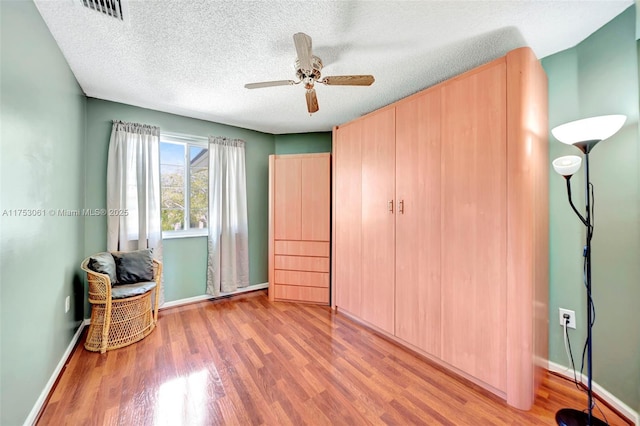 unfurnished bedroom with a textured ceiling, ceiling fan, wood finished floors, visible vents, and baseboards