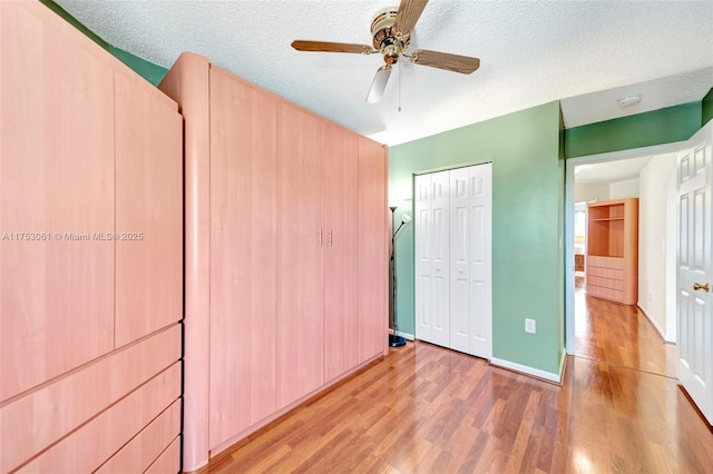 unfurnished bedroom with light wood finished floors, a closet, ceiling fan, a textured ceiling, and baseboards