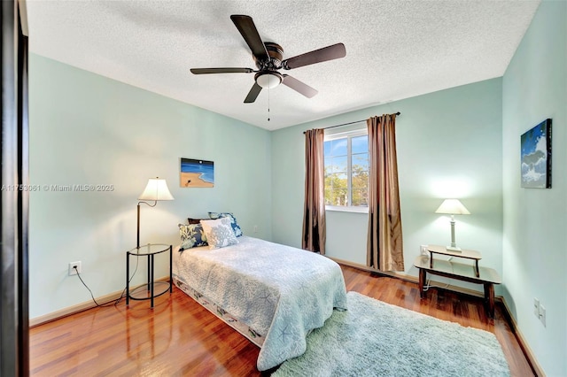 bedroom featuring ceiling fan, a textured ceiling, baseboards, and wood finished floors