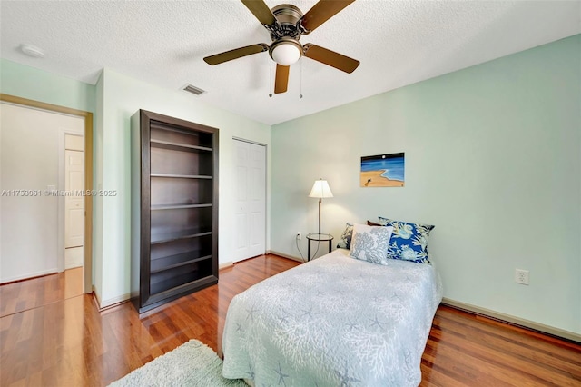 bedroom featuring a textured ceiling, wood finished floors, visible vents, a ceiling fan, and a closet