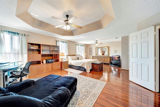 bedroom featuring built in desk, a tray ceiling, a textured ceiling, and wood finished floors