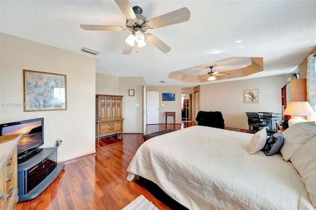 bedroom with a textured ceiling, wood finished floors, visible vents, baseboards, and a raised ceiling