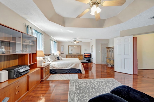 bedroom with ceiling fan, a raised ceiling, and wood finished floors