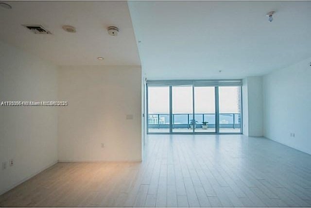 spare room featuring visible vents, a wall of windows, and wood finished floors